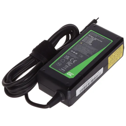 Na zdjęciu znajduje się czarny zasilacz do laptopa z zieloną etykietą zawierającą specyfikacje techniczne. Kabel zasilający jest zwinięty i zabezpieczony rzepem.