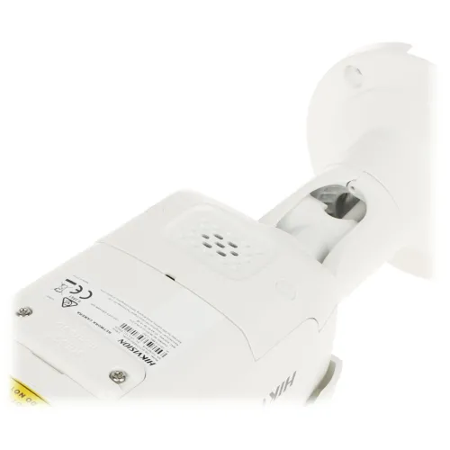 Zdjęcie przedstawia biały głośnik z widocznymi oznaczeniami i etykietami na obudowie. Głośnik ma cylindryczny kształt i jest zamontowany na uchwycie ściennym.