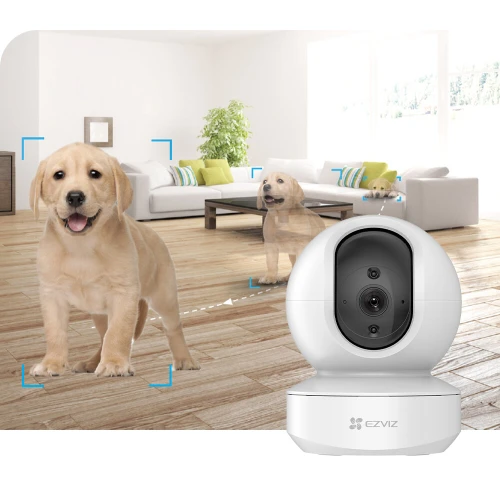 Kamera IP EZVIZ TY1 w kolorze białym, o nowoczesnym, zaokrąglonym designie, umieszczona w jasnym wnętrzu. Produkt oferuje funkcję śledzenia ruchu, co ilustruje obraz szczeniaka w salonie.