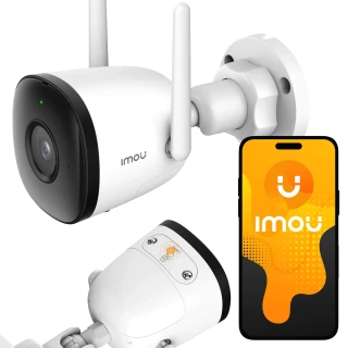 Na zdjęciu znajduje się biała kamera IP Imou z dwoma antenami, zamontowana na ścianie. Obok kamery widoczny jest smartfon z logo Imou na ekranie.