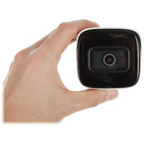 Zdjęcie przedstawia kamerę IP trzymaną w dłoni, ukazującą jej przednią część z obiektywem. Kamera ma kompaktowy, kwadratowy kształt z czarnym frontem i białymi bokami.