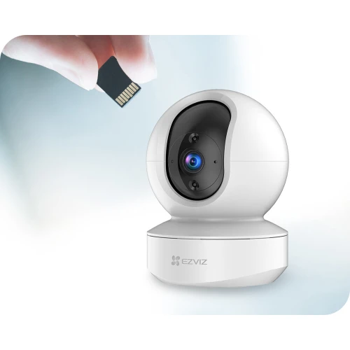 Na zdjęciu znajduje się biała, obrotowa kamera IP Full HD marki EZVIZ o nowoczesnym, kulistym kształcie. Obok kamery widoczna jest ręka trzymająca kartę microSD, sugerująca możliwość rozszerzenia pamięci urządzenia.