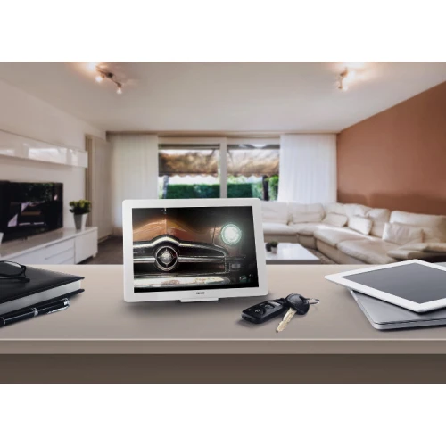 Na zdjęciu znajduje się sterownik gestem Fibaro Swipe, umieszczony na stole w nowoczesnym salonie. Urządzenie ma formę eleganckiej, białej ramki z wyświetlaczem, na którym widoczny jest obraz samochodu.