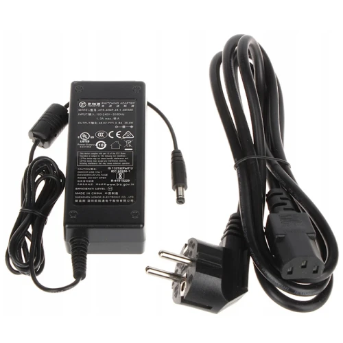 Zasilacz z czarnym kablem zasilającym i wtyczką europejską. Obok znajduje się kabel z okrągłą końcówką do podłączenia urządzenia.