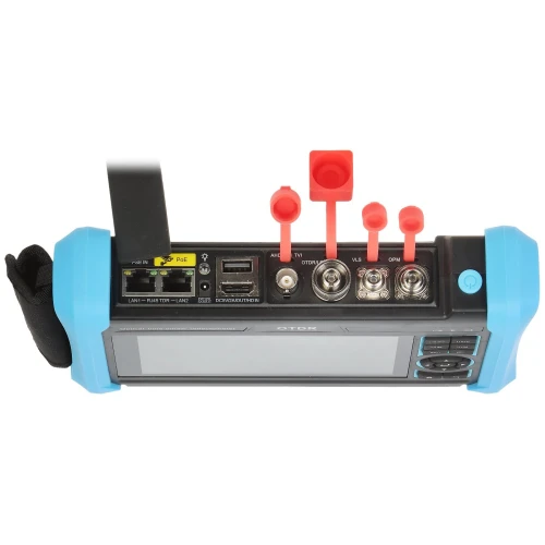 Zdjęcie przedstawia urządzenie pomiarowe z niebieskimi uchwytami i kilkoma portami oraz złączami na górze. Widoczne są różne wejścia, w tym USB, LAN oraz złącza światłowodowe, a także czerwone zaślepki ochronne.